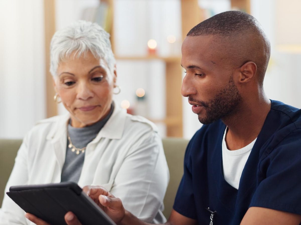 Clinician in navy scrubs helping an older patient complete a form on a tablet
