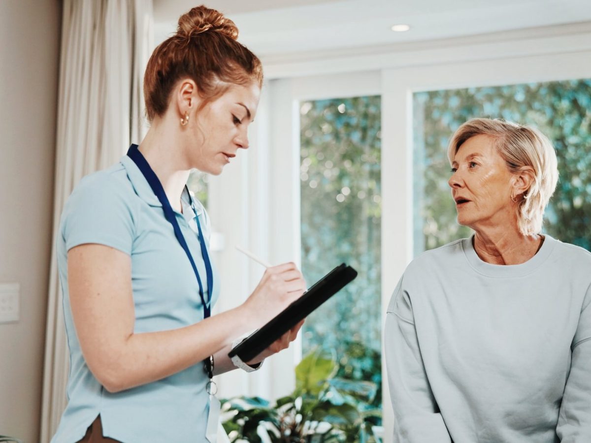 Allied health practitioner taking session notes on a tablet while talking with a client