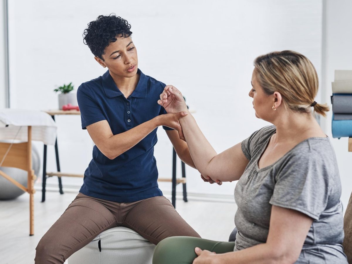 Therapist supporting a client's wrist and elbow while assessing arm movement in a bright clinic